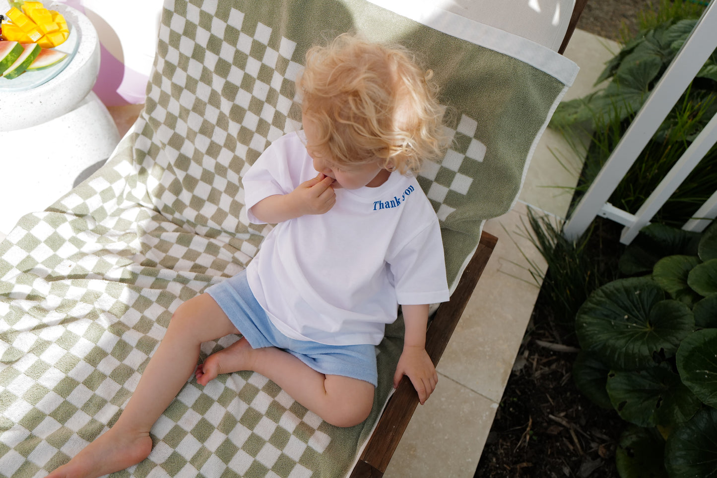 Girl sits  on lounger, view looking down wearing good vibes tee and sky terry shorts