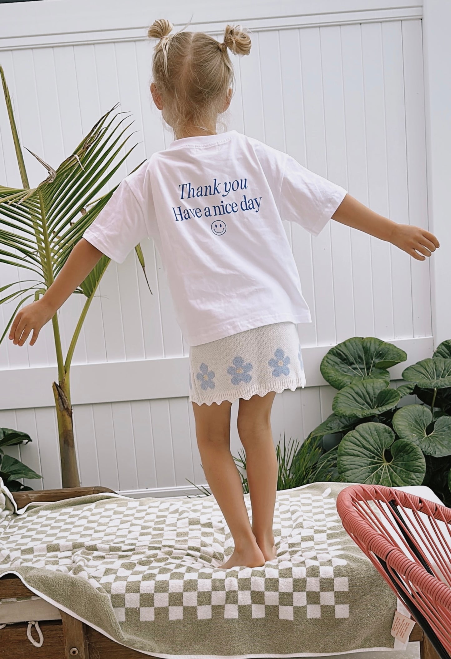 Girl stands on lounger with back to camera wearing good vibes tee and blossom knit dress underneath to show styled as a skirt